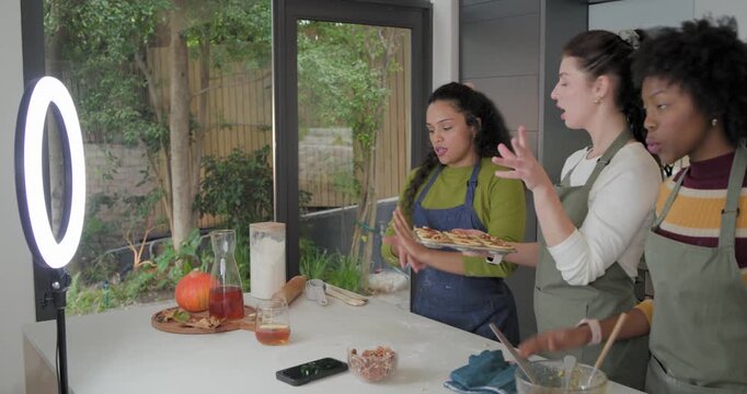 Diverse female friends in aprons posing with tray for ring light phone fetching mitt styling tarts