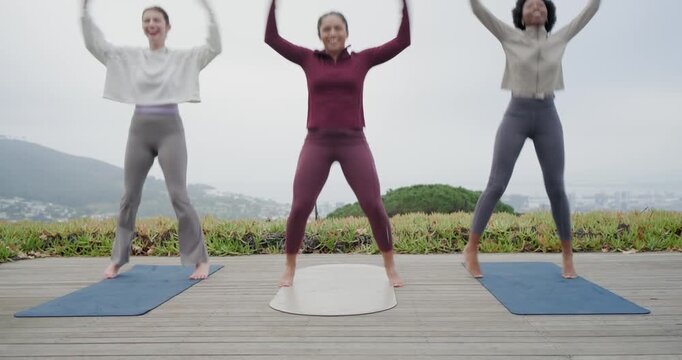 Diverse female friends center-led, doing jumping jacks on deck mats, warming up, stopping laughing