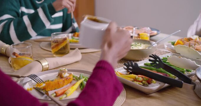 Diverse women starting meal at table, pouring gravy from white pitcher onto roasted squash plates