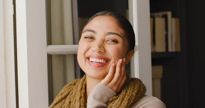 African American woman reacting to off-camera cue, smiling and laughing by window with chunky scarf