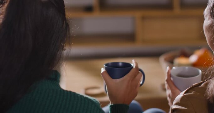 African American woman in green top holding mug turning smiling after companion's comment on sofa