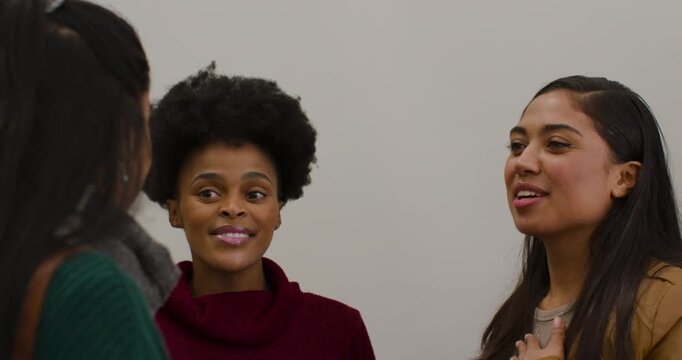 Diverse female friends at gray wall center woman praising right woman placing hand to chest pendant