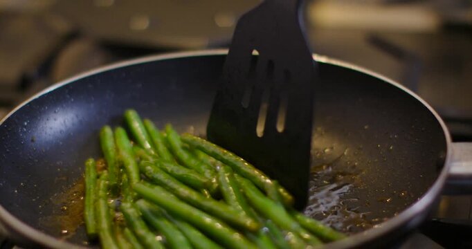 Spatula is touching beans, stirring and flipping them in oil on gas stovetop, pressing to brown