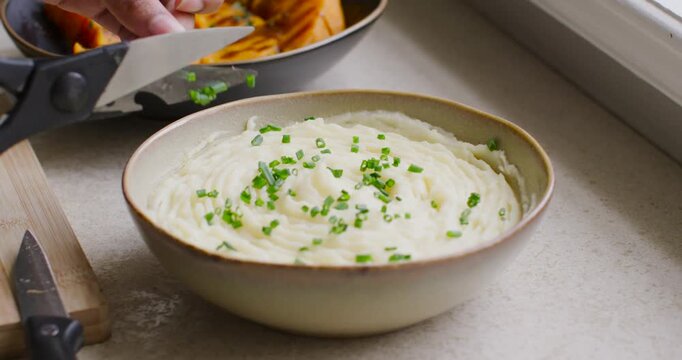 Cook hands in green knit entering left with shears snipping chives plating mashed potatoes, tubers