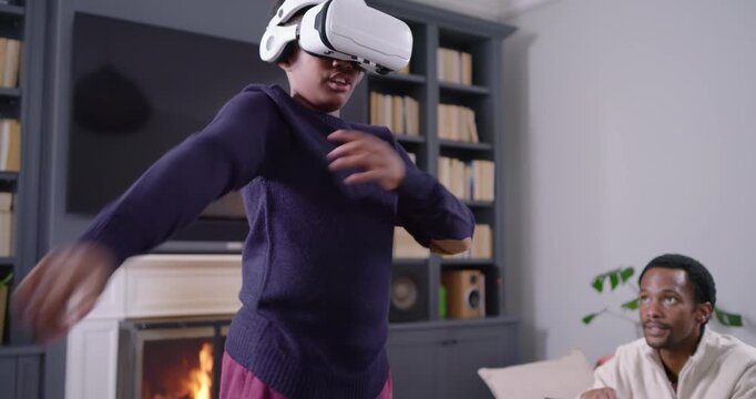 African American family at home parent with tablet watching youth donning white VR headset to play