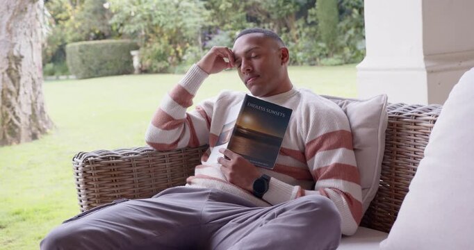 African American man reading ENDLESS NIGHTS, rubbing forehead, reclining on porch for rest