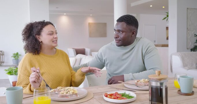 African American couple sitting at wooden table, woman offering orange juice for sip, man clinking