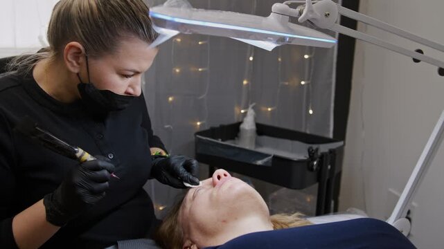 Skilled professional applies intricate eyebrow tattoos using a specialized machine. Close-up view highlights precision and care during this cosmetic procedure for beautiful brows