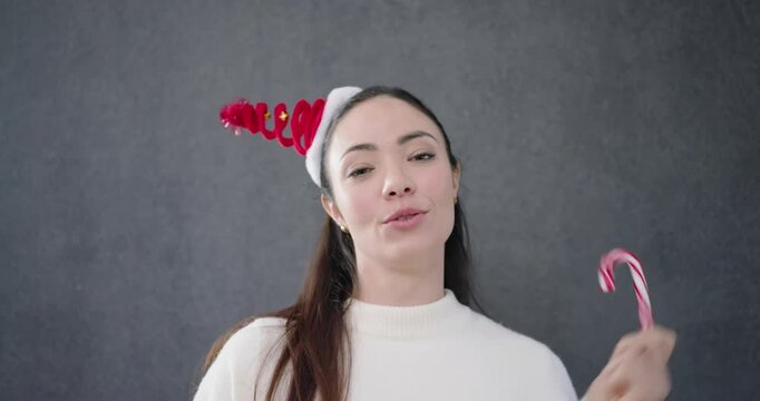 Asian woman in studio holding candy cane, winking, biting and presenting headband for festive pose