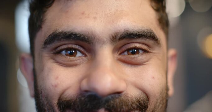 Man holding eye contact with camera, blinking and gradually smiling for studio portrait with bokeh