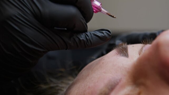 Skilled hands expertly apply eyebrow tattooing using a needle machine. The process includes precision, care, and artistic design, enhancing the natural beauty of the client's facial features