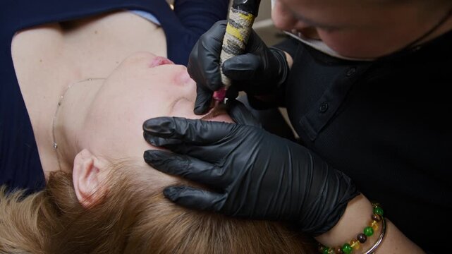 A skilled artist enhances a woman's brows using a precise tattoo machine in a cozy beauty salon. The process involves careful application and meticulous cleanup for stunning results