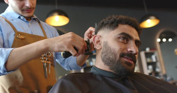 Barber and African man client leaning right receiving fade cut in barbershop with clippers and comb