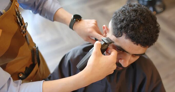 Barber placing clippers at temple, trimming hairline on man in barber chair, refining fade