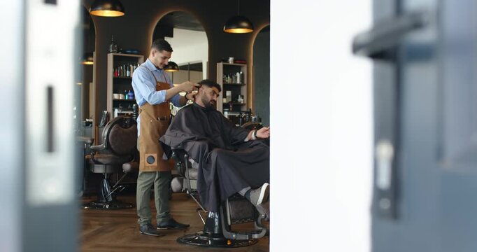 Positioning clippers African American barber cutting male client hair, blending sides at barbershop