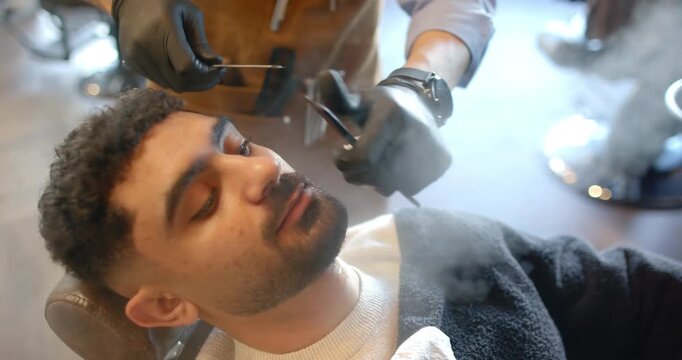 Barber shaving mustache and edging beard on client reclining in barber chair with straight razor