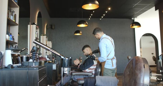 African American male barber walking up, donning gloves, using trimmer, shaping nape in shop
