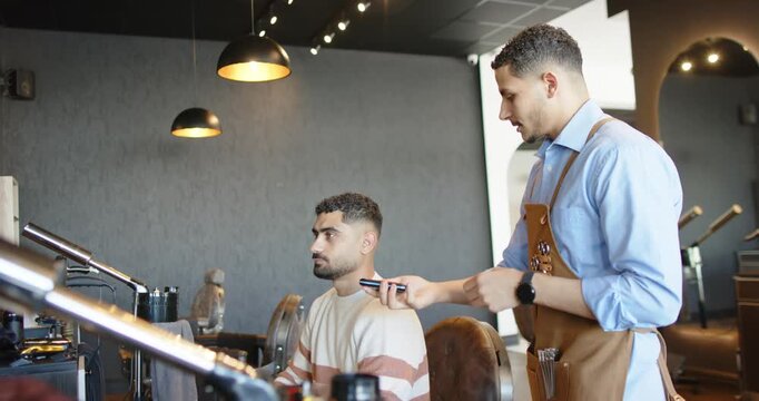 African American barber checking phone, offering reader while client tapping phone to pay at salon