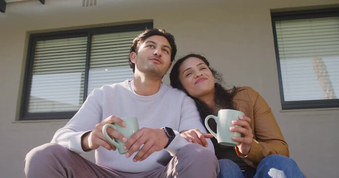 African American couple sitting on stoop gazing with pale green mugs leaning chatting and laughing