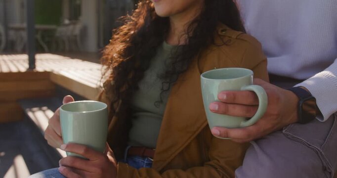 Couple sitting on deck holding mint mugs, sunlight moving causing camera revealing tan coat showing