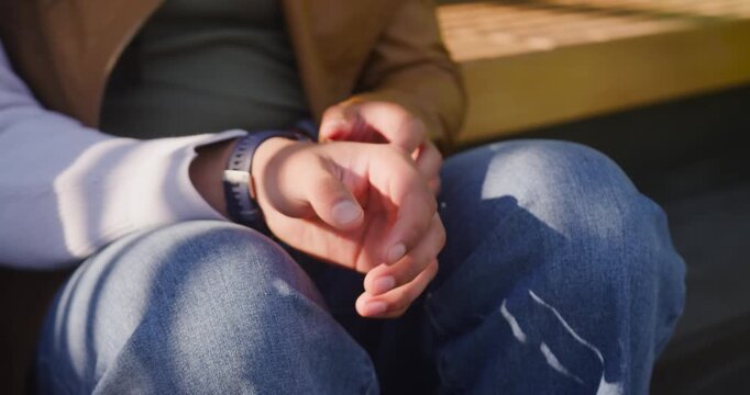 African American woman on bench rubbing fingers interlacing clasping hands with sunlight shifting