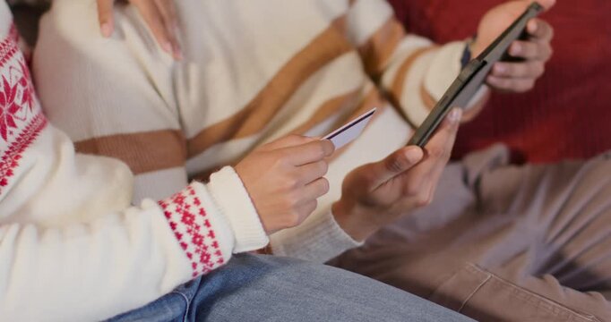African American couple on sofa, woman holding card near tablet while man tapping screen confirming