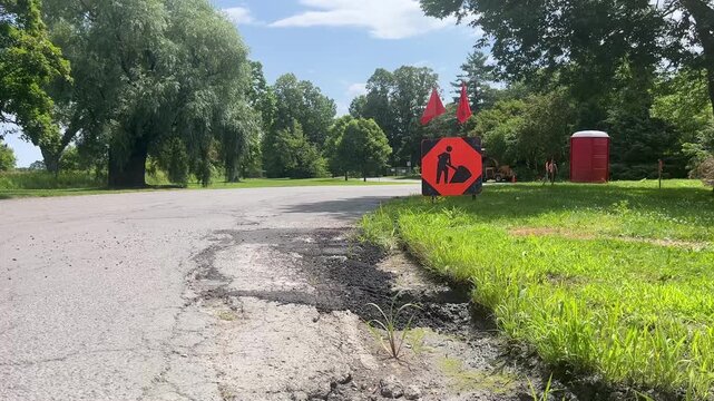 Road work construction sign on grass shoulder next to asphalt pavement
