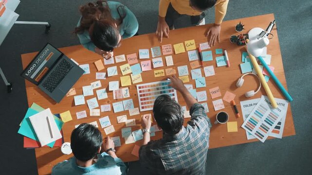 Time lapse of business team with casual outfit looking laptop screen and sharing idea. Aerial view of manager working and checking color palette at table with sticky notes and headphone. Symposium.