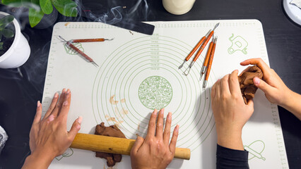 Rolling out brown modeling clay with a wooden rolling pin © Дарʼя Сидорова