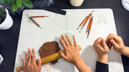 Rolling out brown modeling clay with a wooden rolling pin © Дарʼя Сидорова