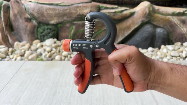 An Asian man is exercising with a hand grip strengthener that has a resistance level of 10 kg.