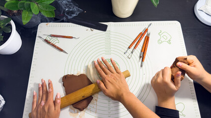 Rolling out brown modeling clay with a wooden rolling pin © Дарʼя Сидорова