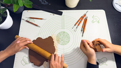 Rolling out brown modeling clay with a wooden rolling pin © Дарʼя Сидорова