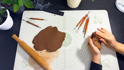 Rolling out brown modeling clay with a wooden rolling pin © Дарʼя Сидорова
