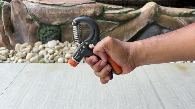 An Asian man is exercising with a hand grip strengthener that has a resistance level of 10 kg.