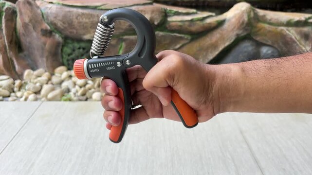 An Asian man is exercising with a hand grip strengthener with a resistance level of 40 kg; his hand trembles as he squeezes the device.