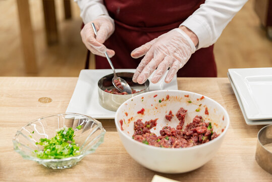 Hands with gloves preparing raw seasoned ground meat in a round mold for food plating and cooking presentation design