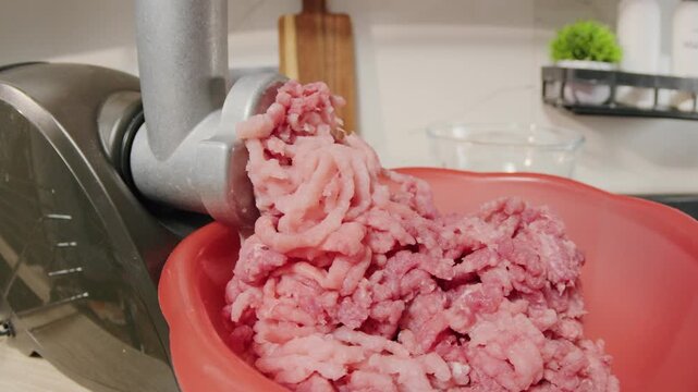 Closeup of meat grinder depositing fresh beef into mixing bowl. Cozy kitchen atmosphere showing beef being minced and collected in bowl for meal preparation