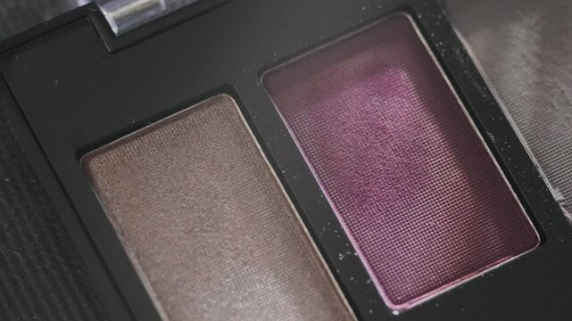 Detailed view of eyeshadow palette with vibrant colors. Editorial flatlay highlighting pigmented purple taupe eyeshadow with shimmering finish and powder details