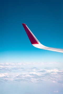 Airplane winglet with red tip against clear blue sky and soft clouds below