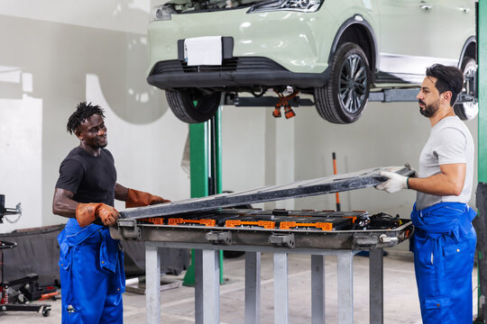 Professional EV technicians preparing to reinstall a high-voltage battery pack during electric vehicle maintenance in a modern service workshop.