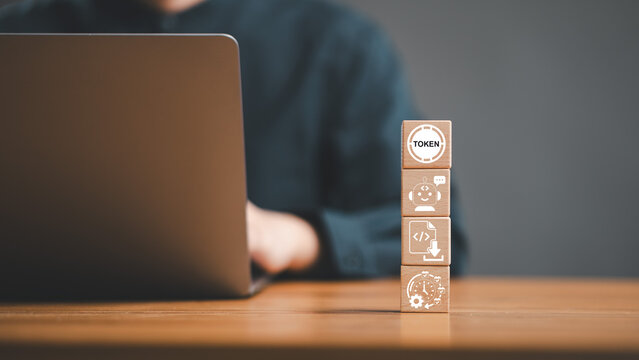 AI language model token usage and chatbot automation cost concept. Wooden cube tower with token chatbot coding and time icons in front of person working on laptop.