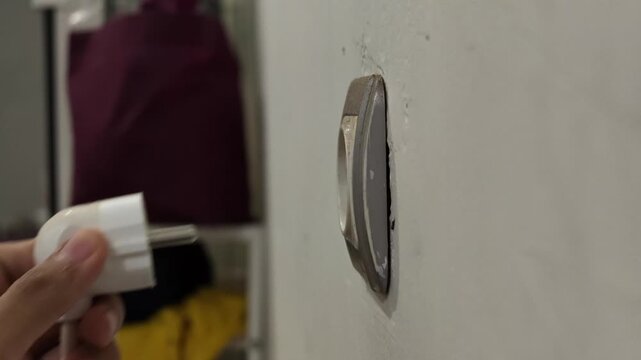 A close up view of a person hand unplugging and plugging a white electric power cable adapter back into a wall socket.
