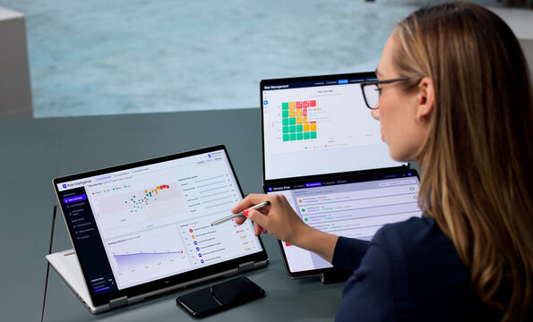 Young Woman Reviews Compliance Data On Dual-screen Laptop