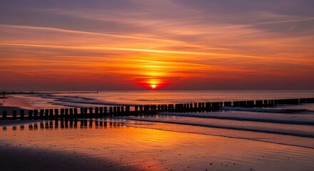 Naklejka premium Sunset over calm beach with wooden pier and reflections.