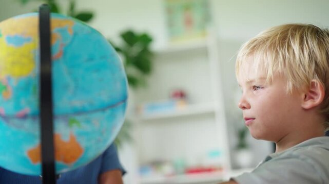 Young preschool boy learning geography using world globe in classroom exploring continents countries and global education during elementary school lesson
