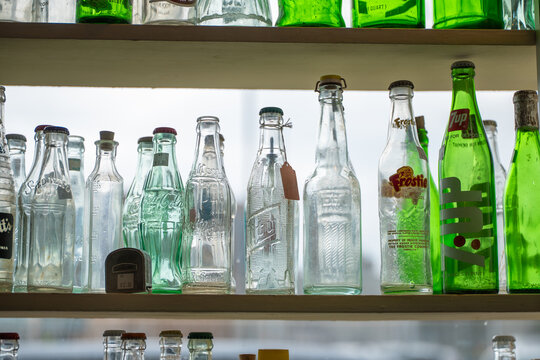 DULUTH, MN - 24 JUN 2026: Vintage glass soda bottles including Coca-Cola, 7-Up and Frostie brands displayed on shelves in a Duluth, Minnesota antique store, backlit by window light.