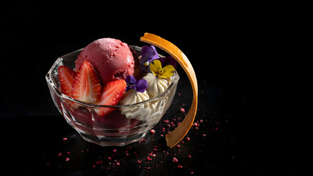 Gourmet berry sorbet dessert in a glass bowl with fresh strawberries, edible flowers, and a crisp tuile garnish on a black background