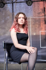 Fototapeta premium A woman with pink hair is sitting thoughtfully on a wooden bench. She is wearing a black dress and dark stockings.