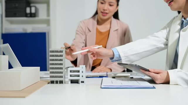 Architects and business professionals review a scale building model during a planning meeting, showcasing architecture, construction, real estate development